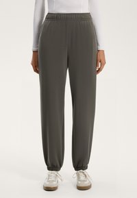 Grå, tapered joggerbyxor med elastisk midja och tappade anklar, tillverkade av ett glättat tyg. Kombineras med vita och beige sneakers.