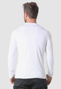 Pitkähihainen valkoinen paita, valmistettu sileästä kankaasta. Siinä on pyöreä kaula-aukko ja vartalonmyötäinen malli, näkyvillä oleva ompelusauma helmassa.