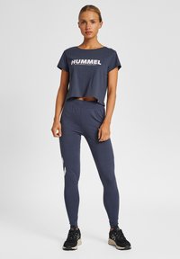 Mörkblå träningsoverall som inkluderar en cropped t-shirt med vit "HUMMEL"-logotyp och matchande högmidjade tights med ljusgrå accenter.