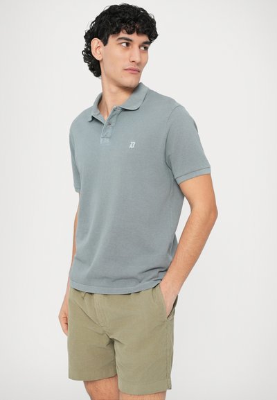 Γκρι κοντομάνικη μπλούζα πόλο με γιακά, με λογότυπο στο στήθος, σε συνδυασμό με ανοιχτοπράσινα σορτς από ελαφρύ ύφασμα.