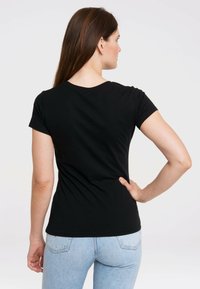 Black fitted t-shirt with short sleeves, round neckline, and a smooth cotton texture, paired with light blue jeans, viewed from the back.