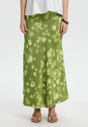 Vihreä kukallinen satiininen midihame, päällä valkoinen toppi ja ruskeat sandaalit, vasemmassa ranteessa rannekorut.