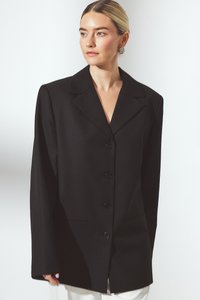 Melnā bleizeris ar strukturētu siluetu, ar izgriezumu jaku, pogu priekšpusi un divām priekšējām kabatām. Gluda auduma ar minimālu tekstūru.