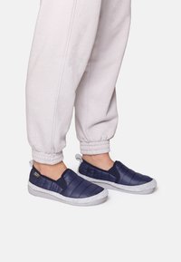 Mornarske slip-on cipele s kvadratnim uzorkom i svijetlosivom gumenom potplatom. Nosene s svijetlosivim trenirkama s manžetama.