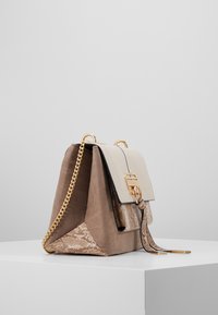 Bolso de ante marrón con una solapa crema, presentando una base de textura en print de serpiente, cadena dorada y cierre de metal.