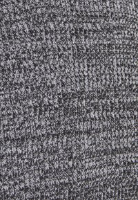 Tissu tricoté dans des tons gris foncé et noir, présentant un motif texturé avec des tailles de points variées. Matière douce et extensible.