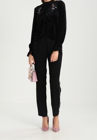 Svart sammetblus med broderade blommor, kombinerad med figurnära svarta byxor med vita ränder. Glittriga rosa klackar och en rosa handväska.