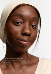 Beige-pohjallinen testiväri tummalla iho sävyllä. Malli käyttää vaalean väriä yläosaa ja kermaista huivia, esitellen luonnollista ihon rakennetta.