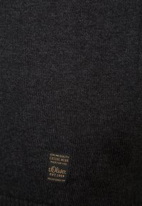 Tissu tricoté gris foncé avec une petite étiquette noire indiquant « Genuine Quality Casual Wear s.Oliver Est. 1969 Registered TM » près du bas.
