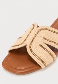 Naturlig fiberslide sandaler med beige tau-detaljer og gullfargede aksenter, med flat brun såle og firkantet tådesign.