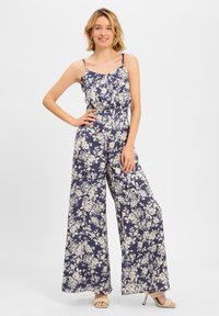 Tuta floreale blu navy con spalline sottili, gamba larga e vita cinchata. Presenta motivi floreali color crema in tutto il capo.