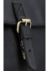 Black leather bag close-up featuring a brass buckle and strap, with visible stitching detail and a smooth textured finish.