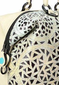 Bolso de mano de cuero color crema con un panel de diseño marrón y verde, adornado con cortes geométricos. Detalle de cremallera en la parte superior con accesorios plateados.