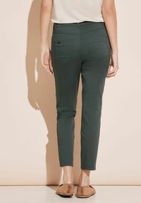 Gröna, åtsittande byxor med en slät textur, två bakfickor och midjehög midja, matchat med bruna slip-on skor.