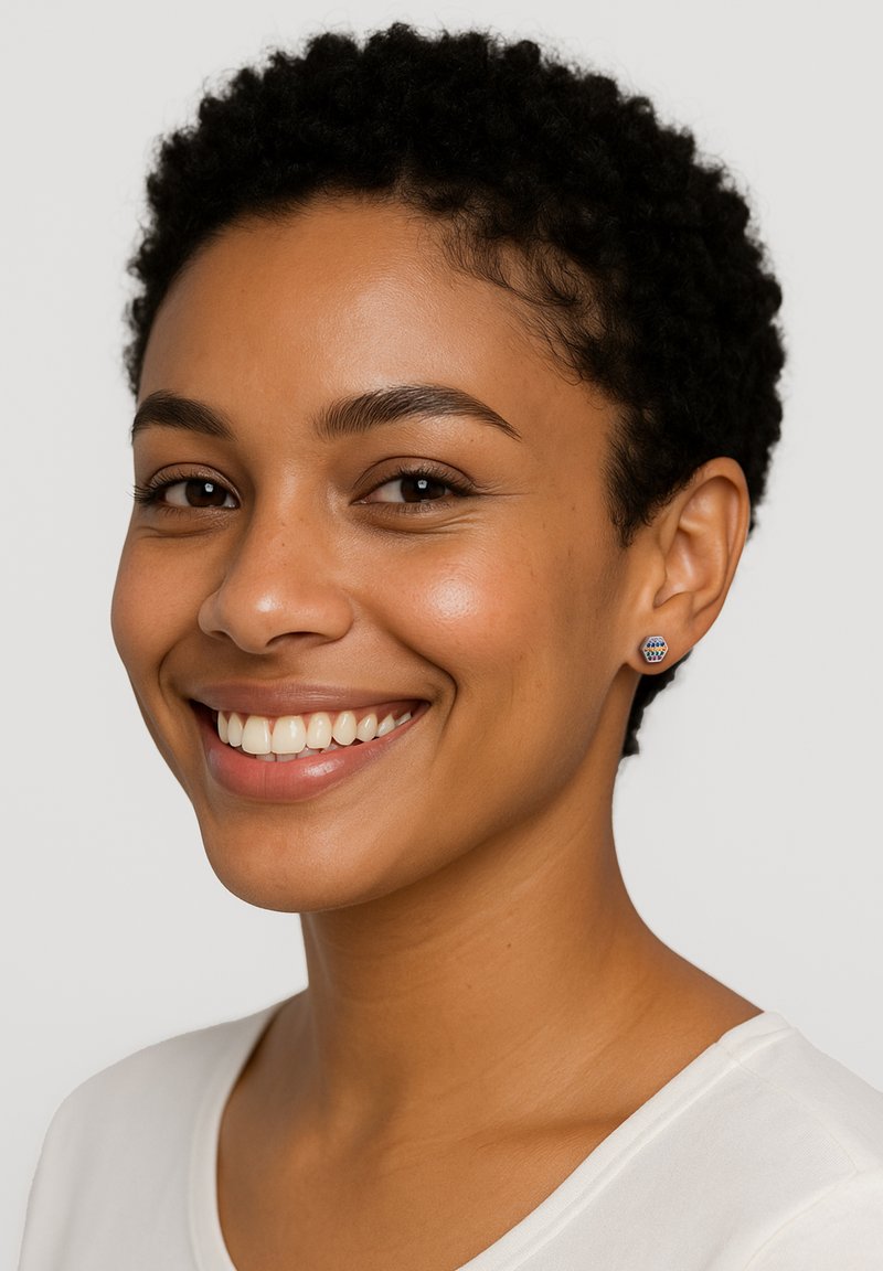 Små blå örhängen med geometriskt mönster, bärs av en modell med kort, lockigt hår och en ljusfärgad topp, som ler.