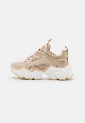 Beżowy masywny sneaker z grubą białą podeszwą, z przodu na sznurówki, z siateczką i skórzanymi detalami oraz pętelkami na języku i pięcie.