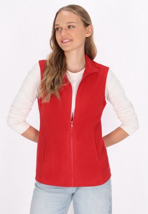 Rote Fleece-Weste mit hohem Reißverschlusskragen, vorderem Reißverschluss und abgerundetem Saum. Getragen über einem hellen Langarmshirt.