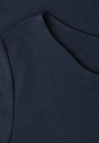 Gros plan sur un tissu bleu foncé montrant des coutures détaillées et des coutures pliées sur un matériau textile doux.