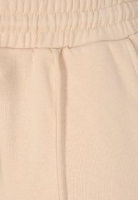 Beige elastisk livrem med en glat tekstur, der har en lægdetalje på siden for ekstra design. Blødt, strækbart stof.