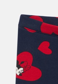 Tumši zils audums ar sarkaniem sirsniņu rakstiem un nelielu karikatūras peles seju ar loku, kas ir izdrukāta pie malas.