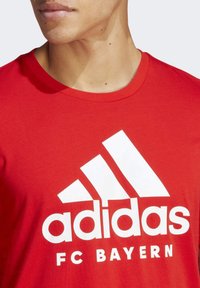 Camiseta de algodón roja con un gran logo blanco de Adidas y el texto "FC BAYERN", escote redondeado y mangas cortas.
