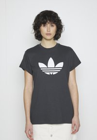 Tamsiai pilka medvilninė marškinėliai su trumpomis, susuktomis rankovėmis, turintys didelį baltą Adidas trefoil logotipą ir tris horizontalias juosteles po juo.