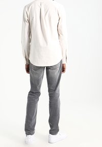 Hellbeiges Hemd mit Knopfleiste und Rückenfalte, kombiniert mit grauen Jeans und weißen Turnschuhen. Glatte Textur, legerer Schnitt und schlichtes Design.