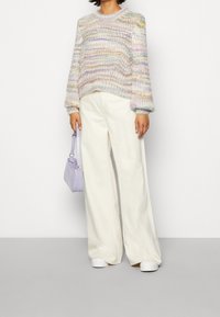 Maglione lavorato a maglia multicolore con maniche lunghe, collo rotondo e vestibilità comoda, abbinato a pantaloni crema a gamba larga e una piccola borsa viola.
