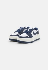Nike madalae spordijalatsid on varustatud valge nahast ülemise osaga, millel on tumesinised aktsendid, struktureeritud pind, lame pael ja paks valge vahepealne küljeline osa.
