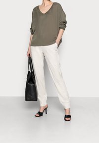 Maglia verde oliva ampia con scollatura a V, abbinata a pantaloni della tuta grigio chiaro. Borsa a tracolla in pelle nera e sandali neri con tacco open-toe.
