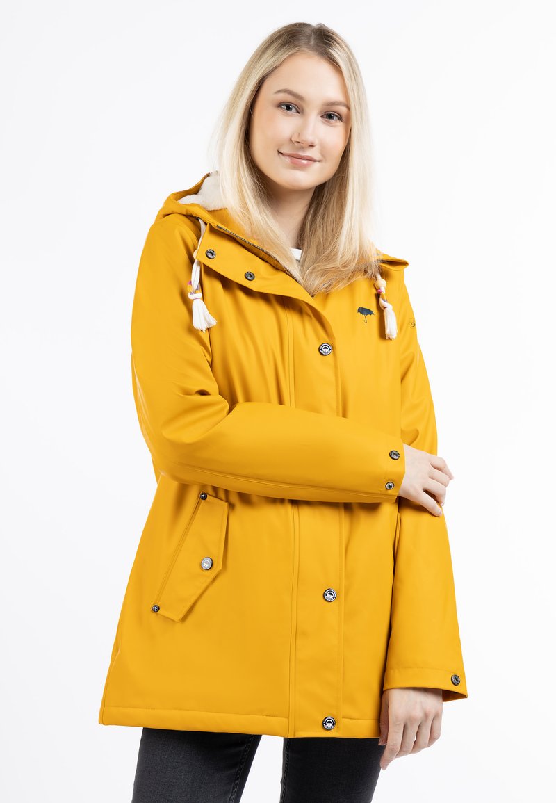 Giacca impermeabile gialla con cappuccio, dotata di bottoni a pressione, due tasche laterali e frange decorative sui lacci. Tessuto liscio.
