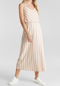 Raidallinen maksimekko, jossa on kerma- ja vaaleanruskea siksak-kuosi, ohuet hihnat ja istuva vyötärö, yhdistettynä valkoisiin tennareihin.