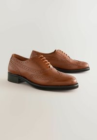 Brown leather dress shoes with perforated wingtip design, pointed toes, and lace-up closure. Black, textured sole adds contrast.