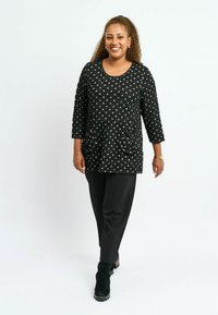 Tunic neagră cu buline alb-negre, dintr-un material texturat, cu mâneci până la trei sferturi, buzunare frontale, asortată cu pantalonii negri și cizme scurte verzi închise.
