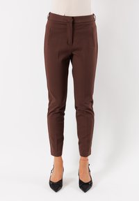 Pantaloni a caviglia slim-fit marroni indossati con tacchi a punta neri su uno sfondo bianco.
