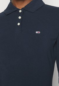 Marineblaues Langarm-Polohemd aus Baumwolle, mit Kragen, drei Knöpfen und einem kleinen bestickten Logo auf der Brust.