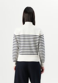 Maglione bianco a maglia con strisce orizzontali blu navy, colletto alto e polsini a coste. Vista posteriore che mostra una silhouette aderente e una texture a contrasto.