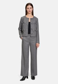 Blazer gris tissé avec des accents de boutons et quatre poches, associé à un pantalon large assorti. Un haut noir et des bottes à talons complètent la tenue.