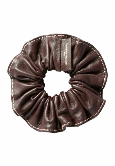 Scrunchie in pelle marrone con texture arricciata e cuciture chiare a contrasto, dotato di un piccolo etichetta cucita sul lato.