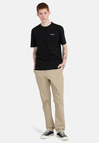 Black cotton t-shirt with short sleeves, crew neckline, and small white logo. Paired with beige pants and black sneakers.