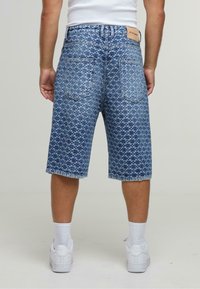 Bermudas de mezclilla con un patrón geométrico azul, de longitud media por el muslo, dobladillo deshilachado, cinco bolsillos y una etiqueta de cuero en la parte posterior de la cinturilla.