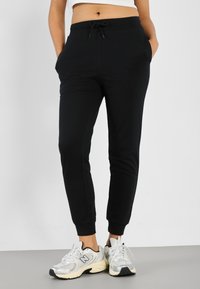 Pantaloni jogging neri con fascia elastica in vita e coulisse, caratterizzati da tasche laterali e polsini affusolati, abbinati a scarpe sportive argentate.