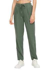 Grüne Leinenhosen mit einem Kordelzugbund, gefältetem Vorderteil, schmal zulaufenden Beinen und seitlichen Taschen, kombiniert mit weißen Sneakers.