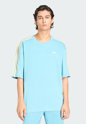 T-shirt in cotone azzurro chiaro con scollo rotondo, maniche corte e design a tre strisce gialle sulle spalle. Presenta un piccolo logo sul petto.