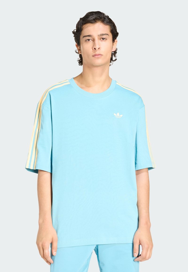 Jasnoniebieska bawełniana koszulka z okrągłym dekoltem, krótkimi rękawami oraz żółtym wzorem z trzema paskami na ramionach. Na piersi znajduje się małe logo.