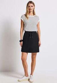 Falda negra con cintura elástica combinada con una blusa blanca de manga corta a rayas. El conjunto se complementa con zapatillas blancas. Textura suave, diseño informal.