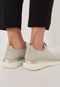 Svetlo béžové pletené topánky na vsúvanie s textúrovaným vzorom, s kovovým akcentom na päte a bielou gumovou podrážkou.