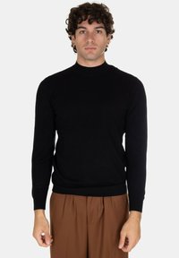Maglione girocollo nero a maniche lunghe realizzato in tessuto morbido. Design aderente con polsini e orlo a costine, indossato con pantaloni marroni.