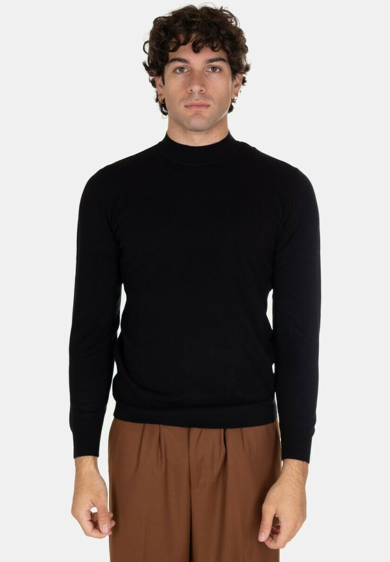 Maglione girocollo nero a maniche lunghe realizzato in tessuto morbido. Design aderente con polsini e orlo a costine, indossato con pantaloni marroni.