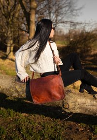 Borsa a spalla in pelle marrone con forma piatta e superficie liscia. Caratterizzata da una lunga tracolla regolabile e dettagli di design minimalisti.